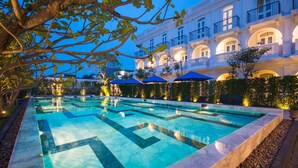 A large outdoor swimming pool with multiple lanes, surrounded by a well-maintained garden and a grand building with balconies. - Little Nyonya Hotel (Wichit)