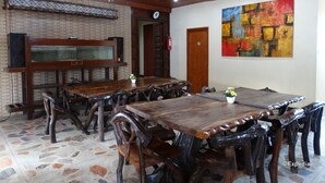 A dining area with wooden tables and chairs, a chandelier, a brick wall, and a colorful abstract painting. - Circon Businessman's Inn (Puerto Princesa)