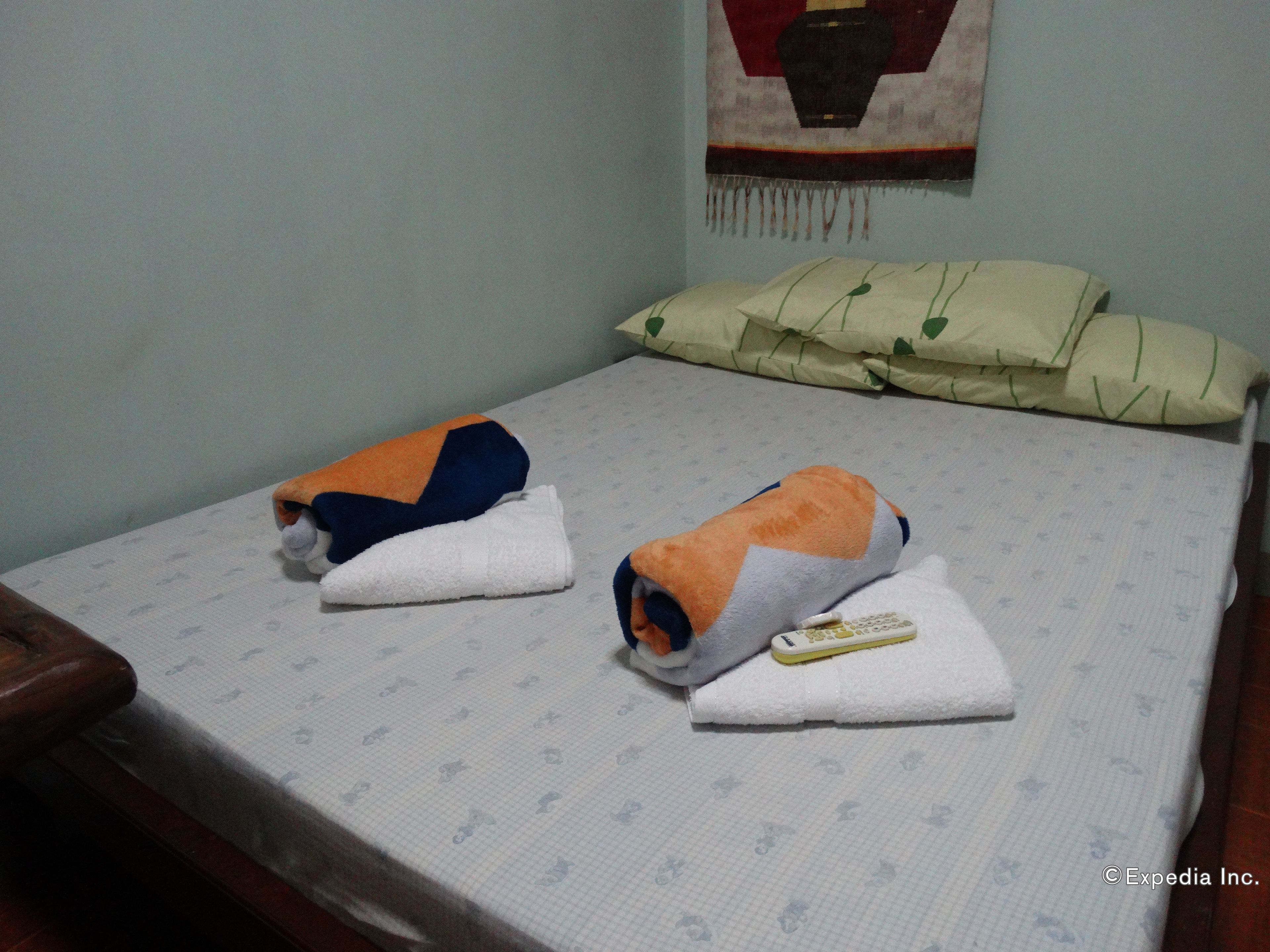 A small bed with a patterned bedspread, two towels, and a remote control on it.