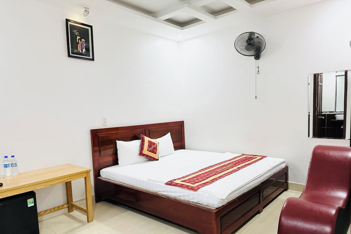 A neatly arranged hotel room with a wooden bed, a red chair, a small desk, and a ceiling fan.