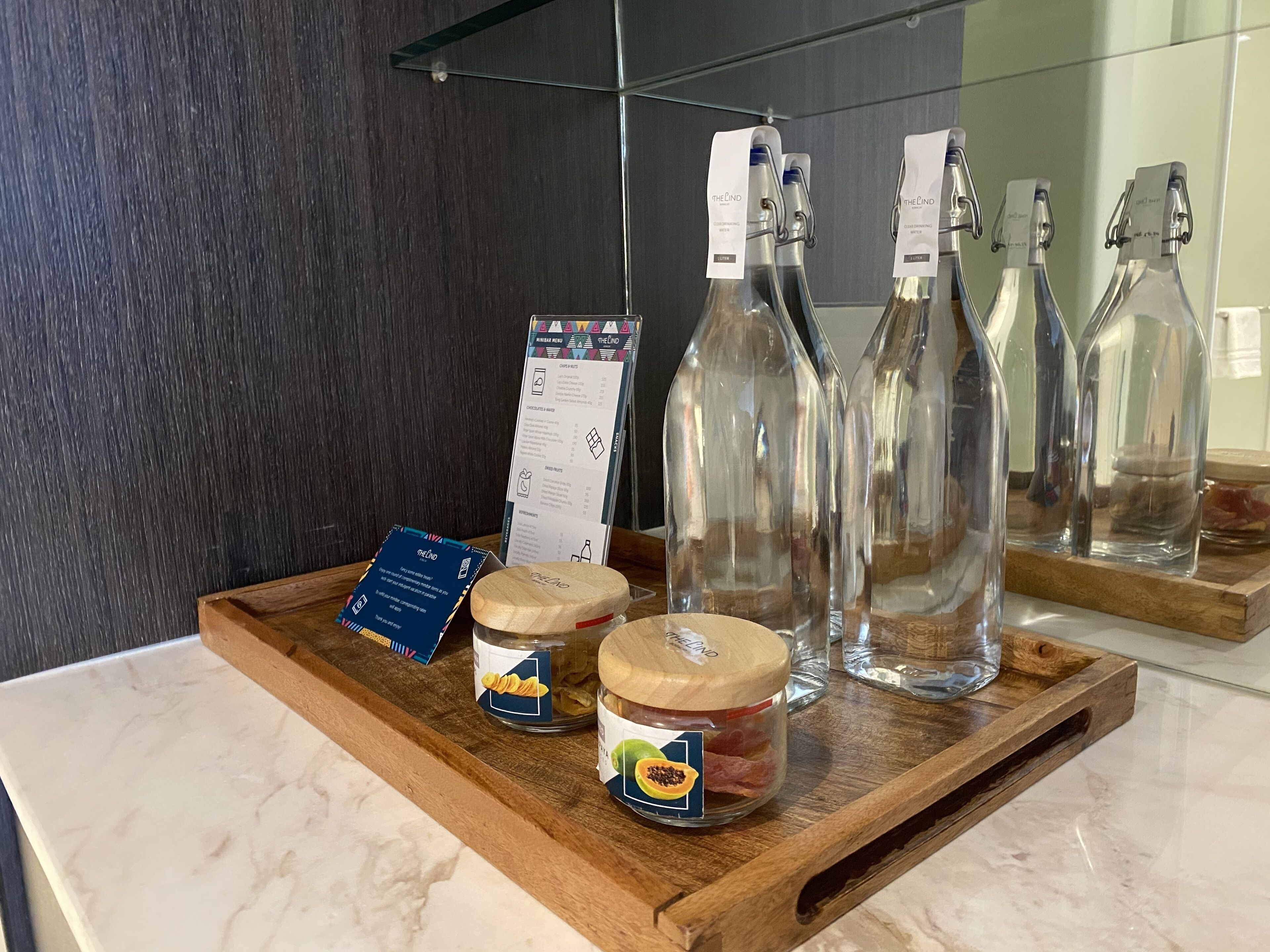 Una bandeja de madera con frascos de aperitivos, un menú y botellas de vidrio vacías sobre una encimera de mármol.