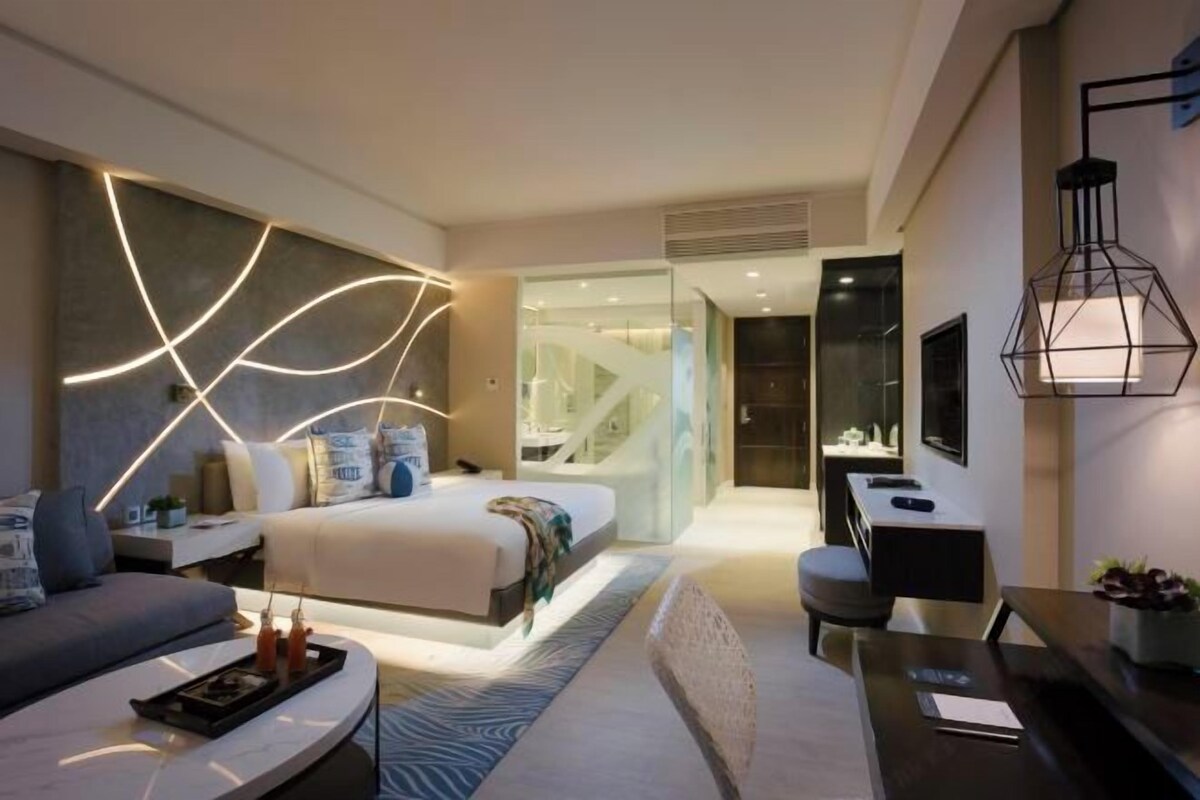 A modern hotel room with a bed, seating area, and a desk.
