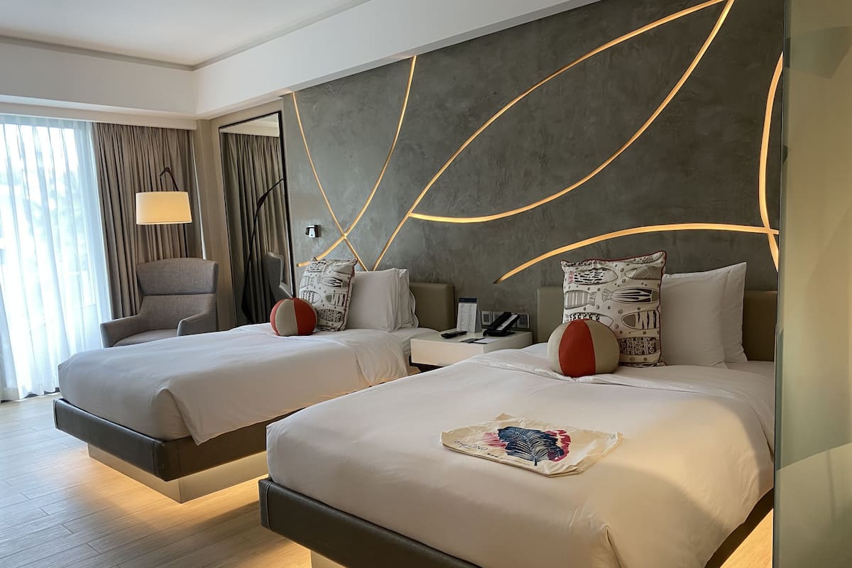 A modern hotel room with two beds, a desk, and a chair.