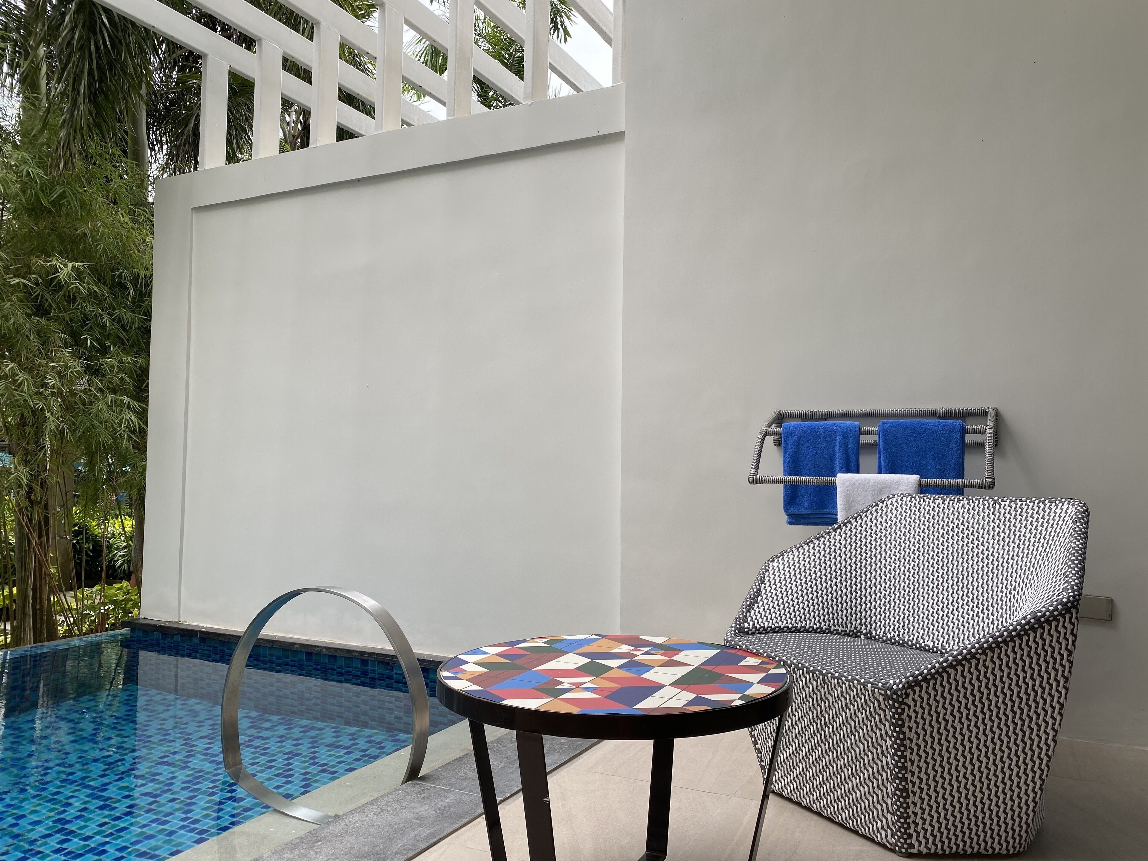 A poolside area with a tiled pool, a round table, and a wicker chair.