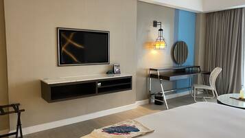 A hotel room with a flat-screen TV mounted on the wall, a desk with a chair, a bedside table, and a bed.