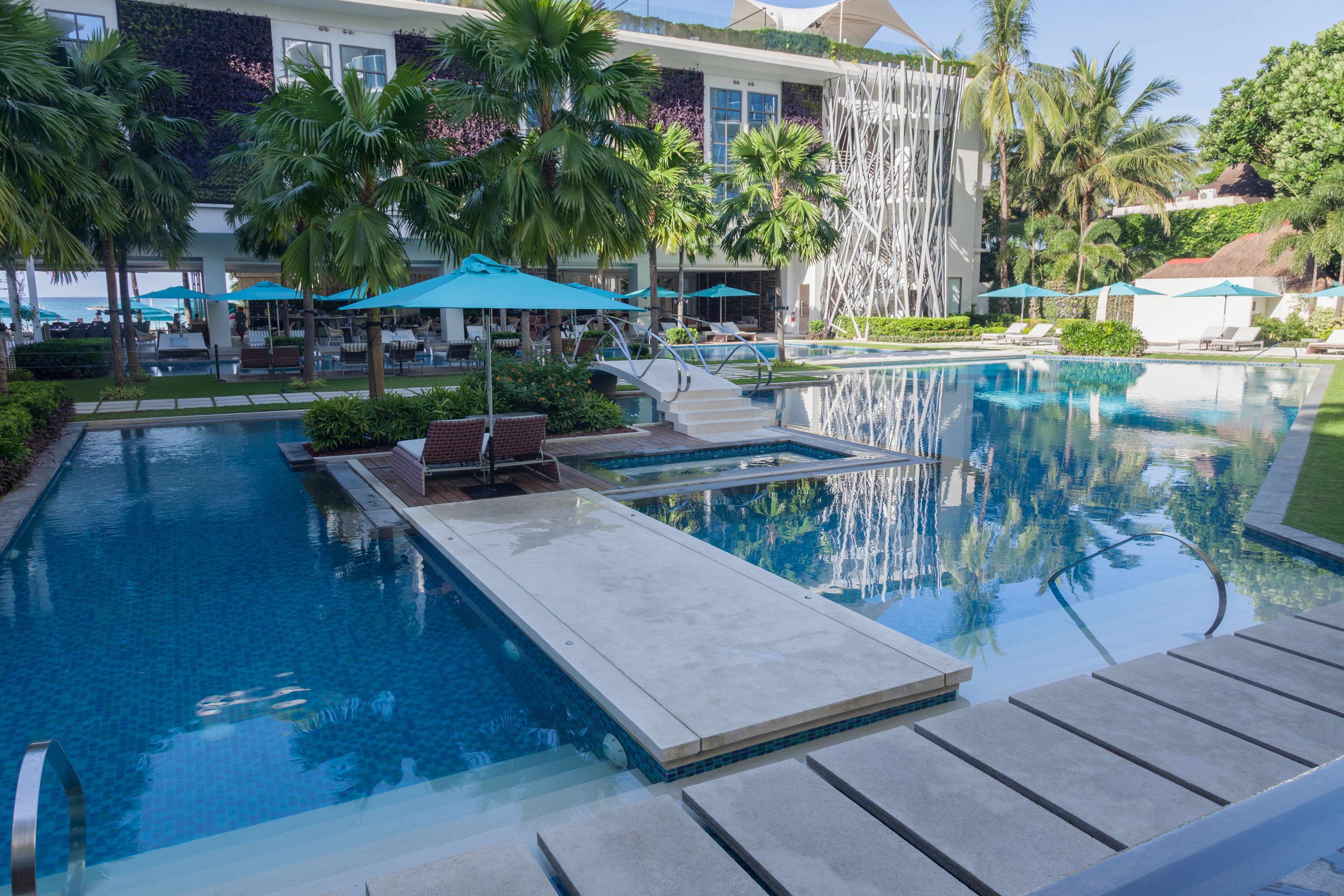 Un espace piscine aménagé dans un complexe hôtelier, avec des chaises longues, des parasols et une cascade décorative.