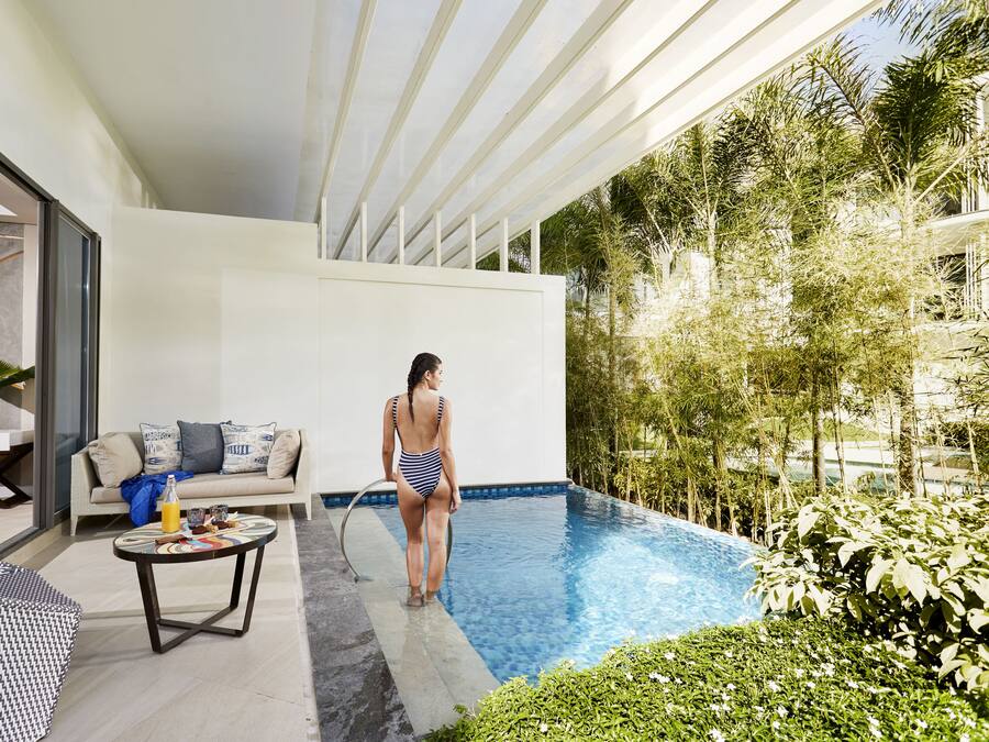 Un área de piscina moderna al aire libre con una persona en traje de baño, un sofá y una mesa con bebidas.