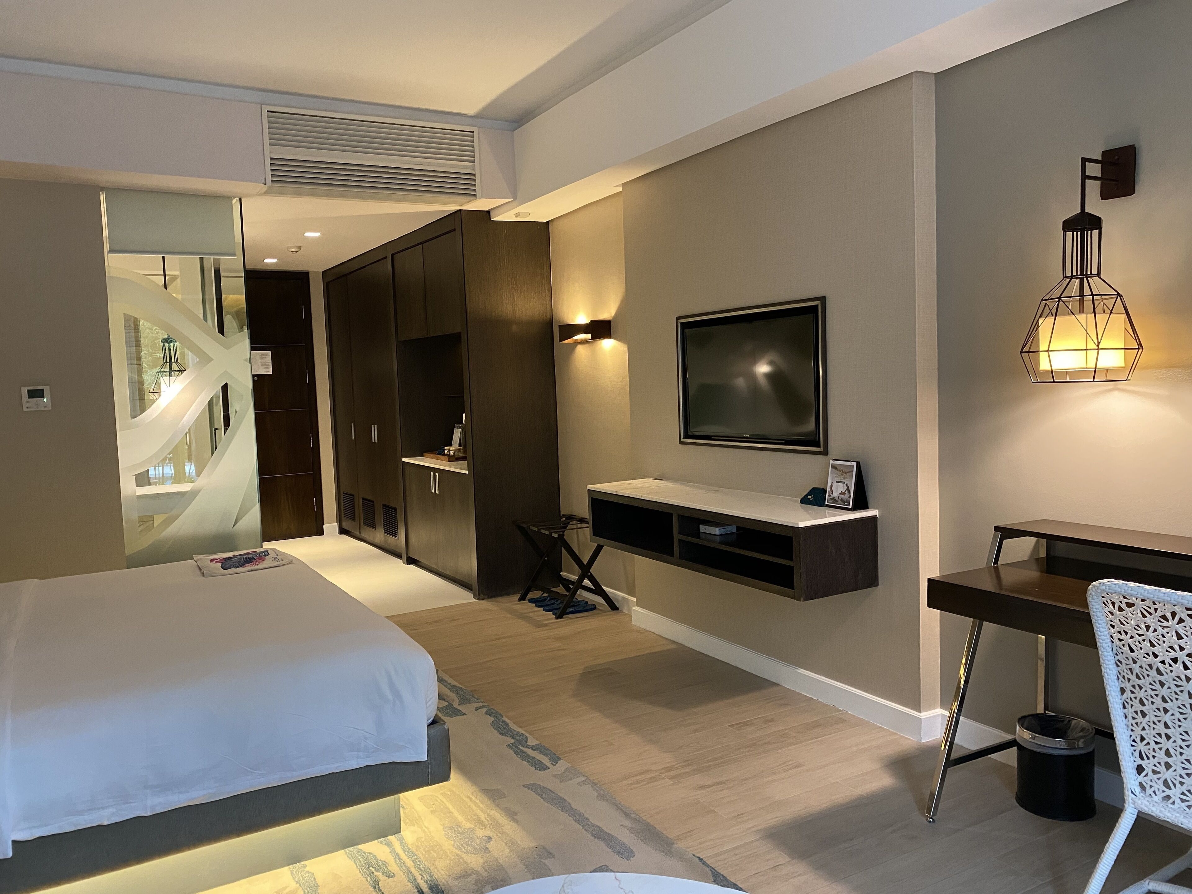 A modern hotel room with a bed, a desk, a TV, and a wardrobe.