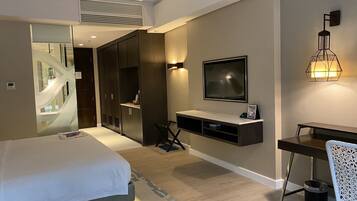 A modern hotel room with a bed, a desk, a TV, and a wardrobe.