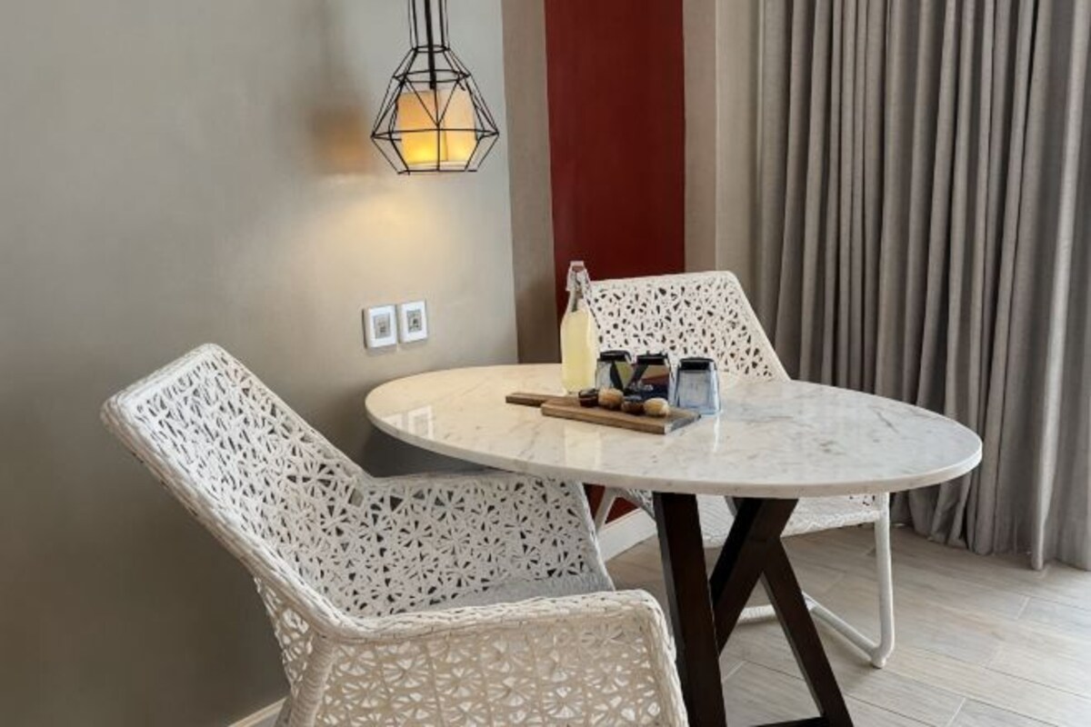 A round table with two white chairs, a bottle, and a small container on it.