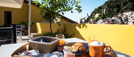 A breakfast tray with croissants, coffee, and juice on a table with a view of a coastal town.