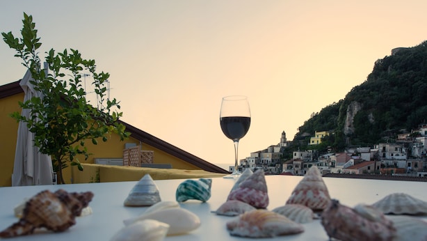 Une table ornée de coquillages et un verre à vin, avec vue sur une ville côtière, ses bâtiments et une colline.