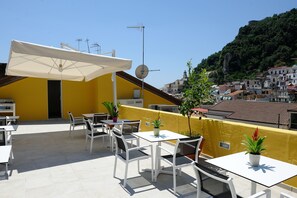 Eine Terrassengruppe im Freien mit weißen Tischen und Stühlen, einem großen Sonnenschirm und Blumentöpfen.
