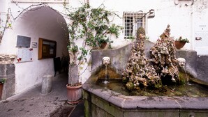 Un bâtiment historique doté d’une fontaine, d’une enseigne indiquant « SUPPORTICO RUA » et d’une fenêtre avec des vitres grillagées.