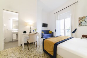 A hotel room with a bed, a desk with a lamp, a sofa, and a television.