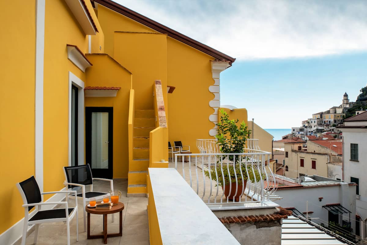 Ein gelbes Gebäude mit einem Balkon, weißen Stühlen, einem kleinen Tisch mit Getränken und einem Blumentopf.