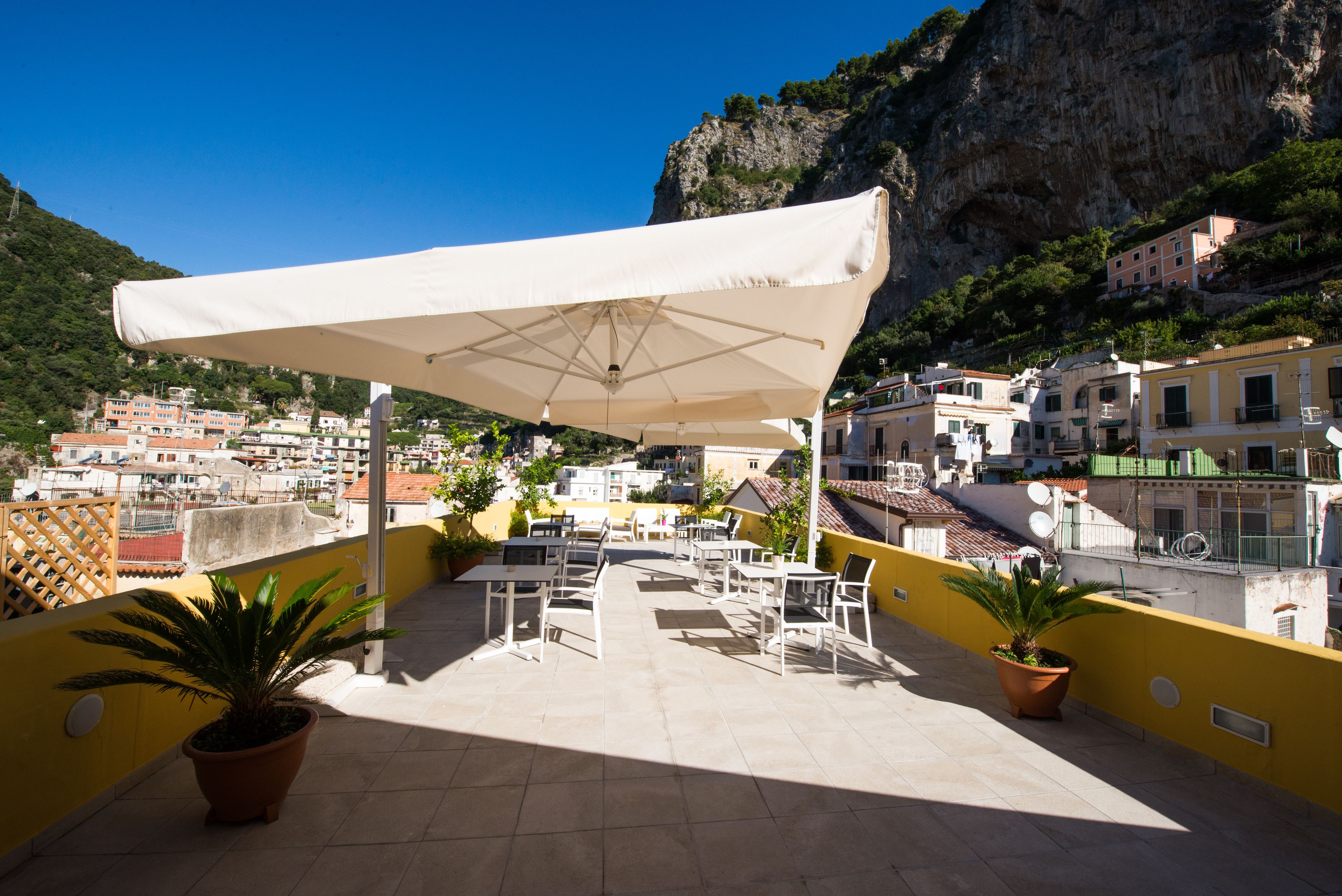 A terrace with outdoor seating, potted plants, and a view of a coastal town and cliffs.