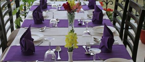 A table set for four with purple napkins, white plates, and a vase with flowers.