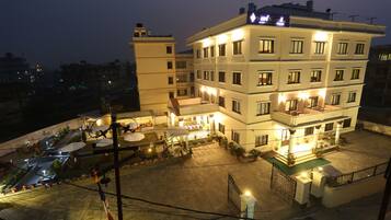 Un hotel de varios pisos con un patio, mobiliario exterior e ingreso bien iluminado.