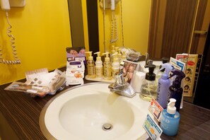 Un baño de hotel con lavamanos, artículos de aseo e un teléfono.