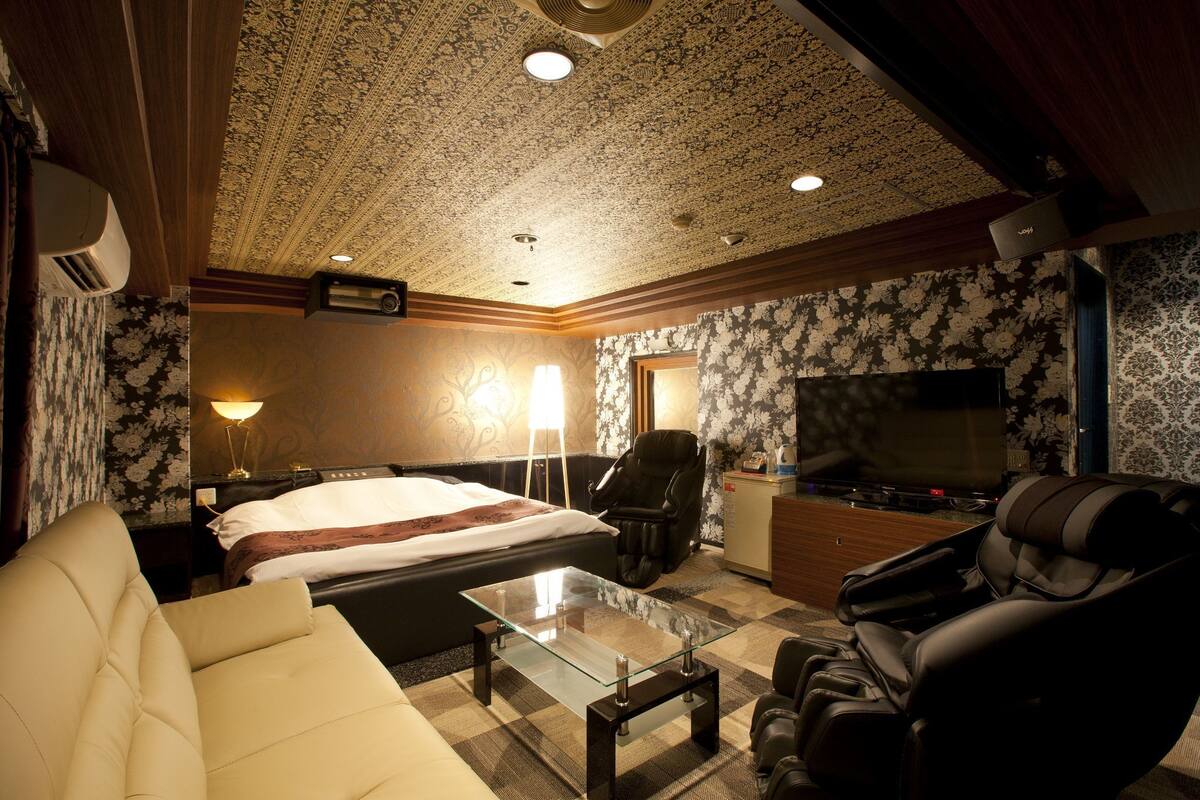 Ein Hotelzimmer mit Bett, einer Sitzecke, einem Massagesessel, einem Fernseher und einem Schreibtisch mit Lampe.