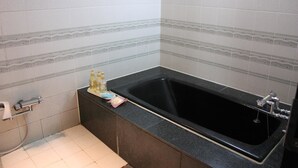 A bathroom with a black bathtub, a toilet, and a sink with toiletries. - Hotel Dessert Hills - Adults only (Kyoto)