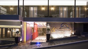 Het uiterlijk van Hotel Sidimos met een opvallende ingang, een balkon en een goed verlichte gevel.