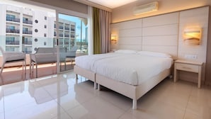 A modern hotel room with a large bed, a small bedside table, a chair, and a view of the city through a large window. - Bull Escorial & Spa (San Bartolomé de Tirajana)