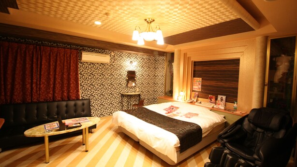 Habitación de hotel con cama, sillón de masaje, mesa y pared con diseño.