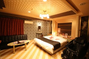Habitación de hotel con cama, sillón de masaje, mesa y pared con diseño.