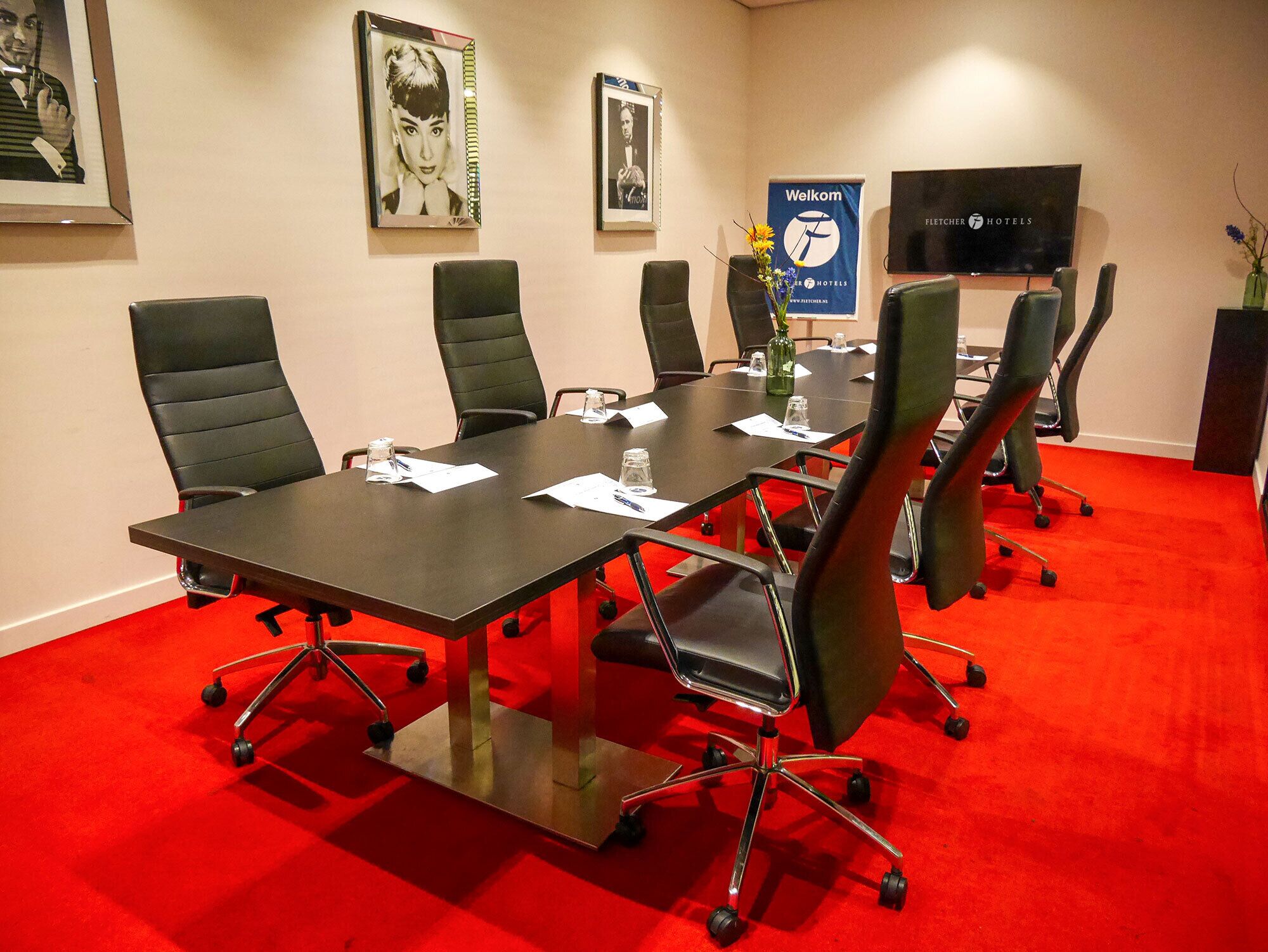 A conference room with a long table, black chairs, a television, and framed pictures on the wall.