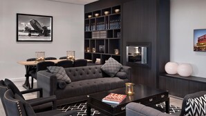 Un salon moderne avec un canapé foncé, des fauteuils, une table basse et une bibliothèque remplie d’objets décoratifs.