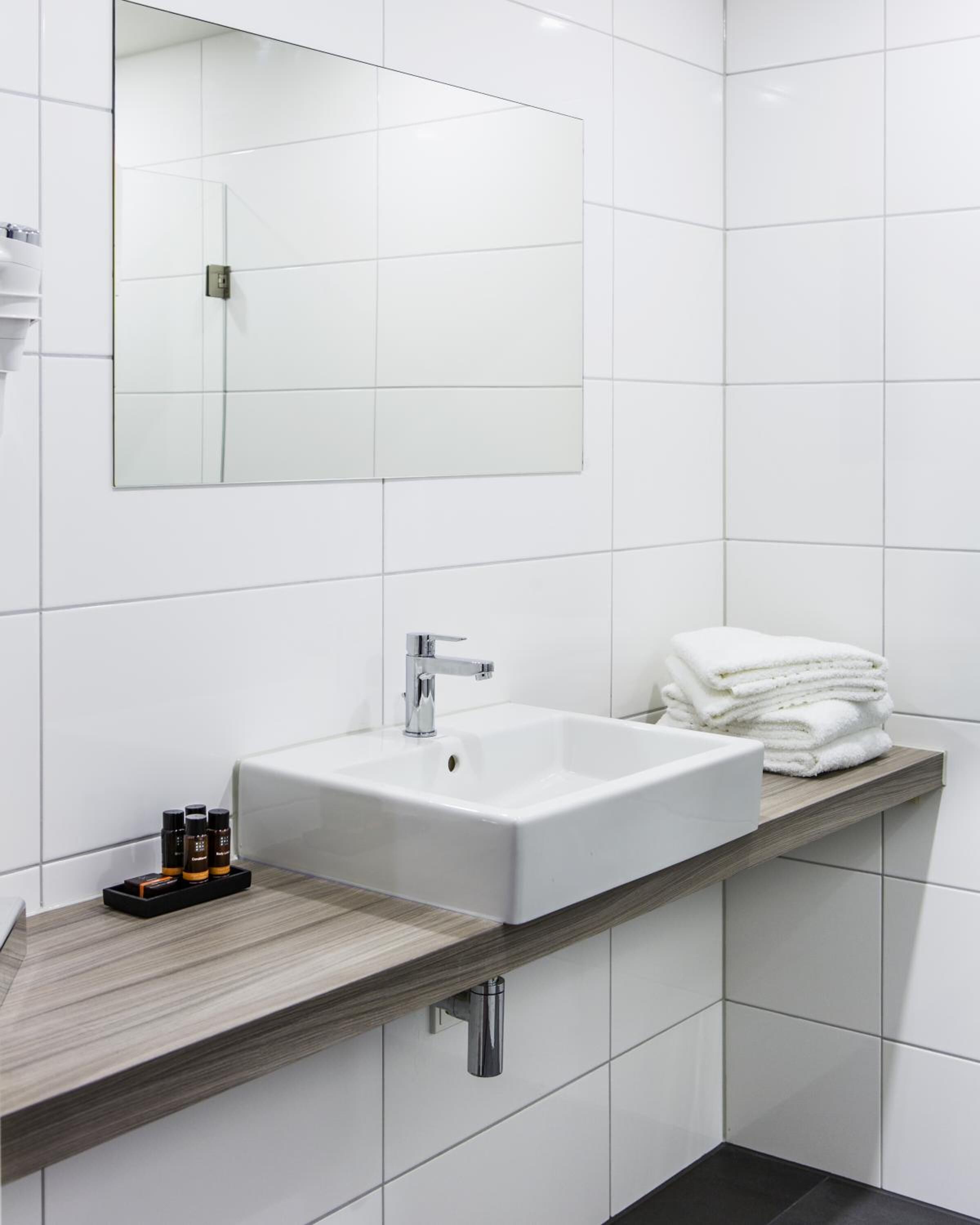 Un baño moderno con lavamanos blanco, espejo y encimera de madera.