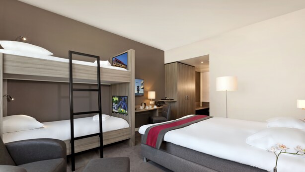 Une chambre d’hôtel avec deux lits, un bureau, une chaise et un petit canapé.