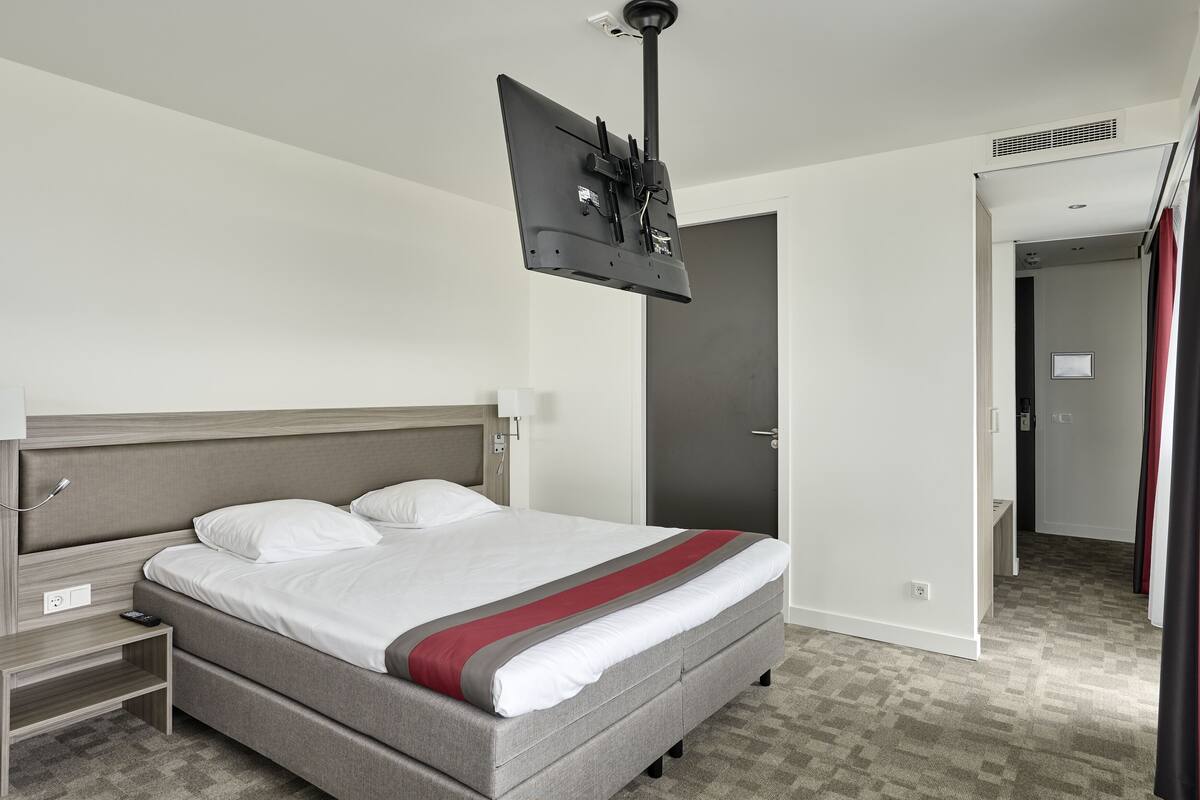 Ein Hotelzimmer mit Bett, Wandfernseher, Nachttisch und Tür.