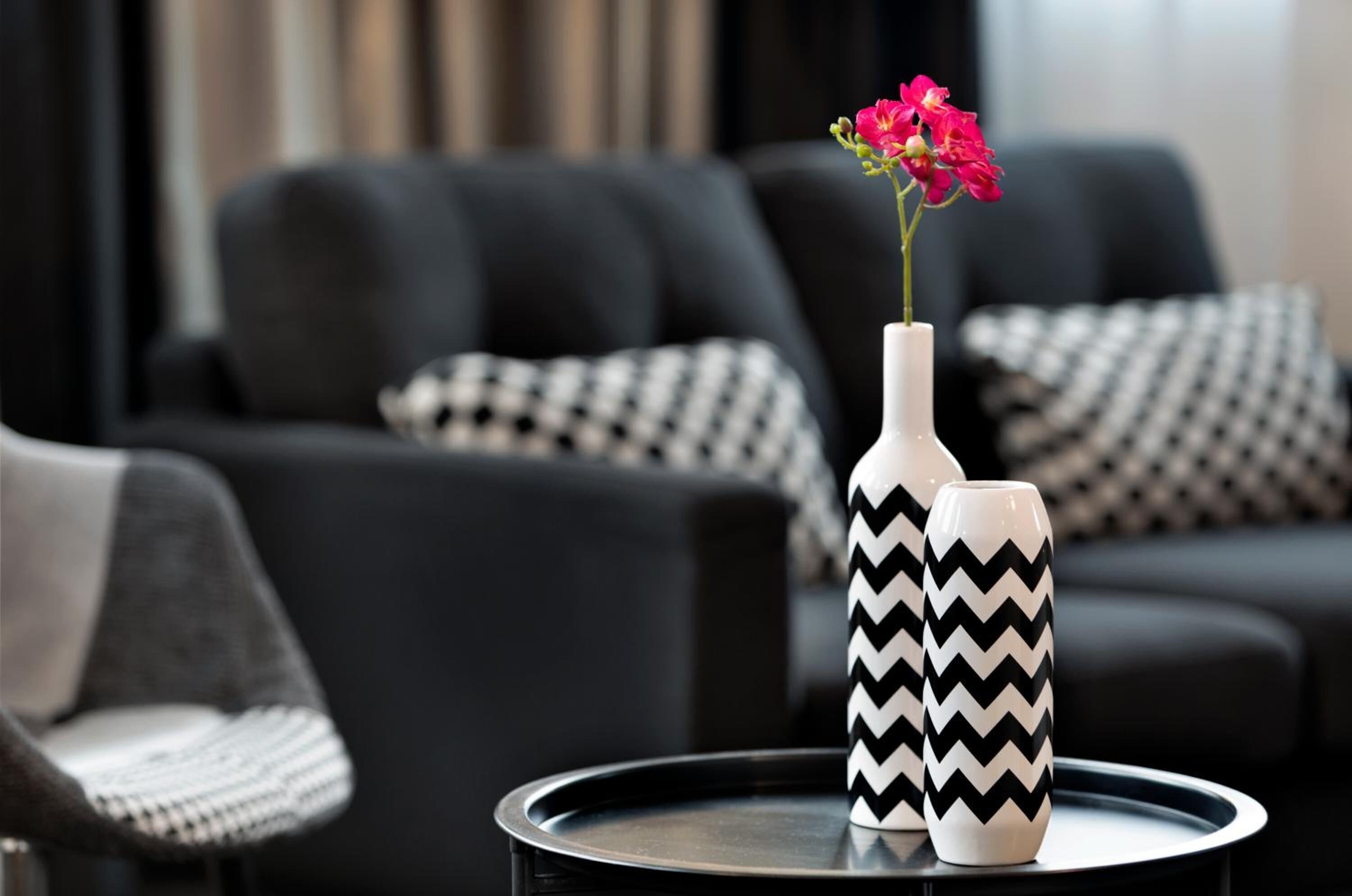 Un soggiorno moderno con un divano a motivi bianchi e neri, un tavolino nero con un vaso bianco e fiori rosa, e una coperta bianca e nera.