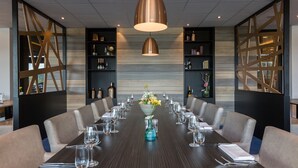 Une salle de conférence avec une longue table, des chaises et un arrangement floral central.