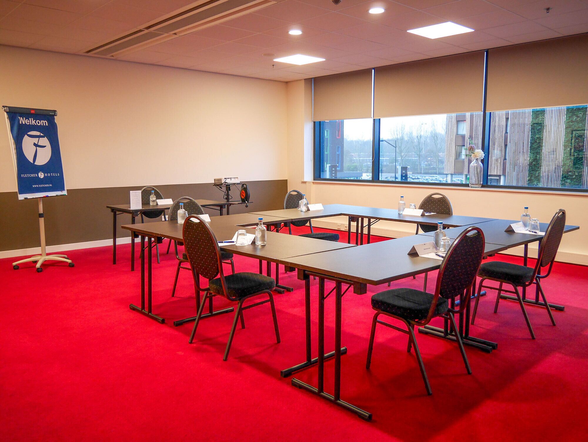 A conference room with tables, chairs, a projector, and a 'Welcome' sign.