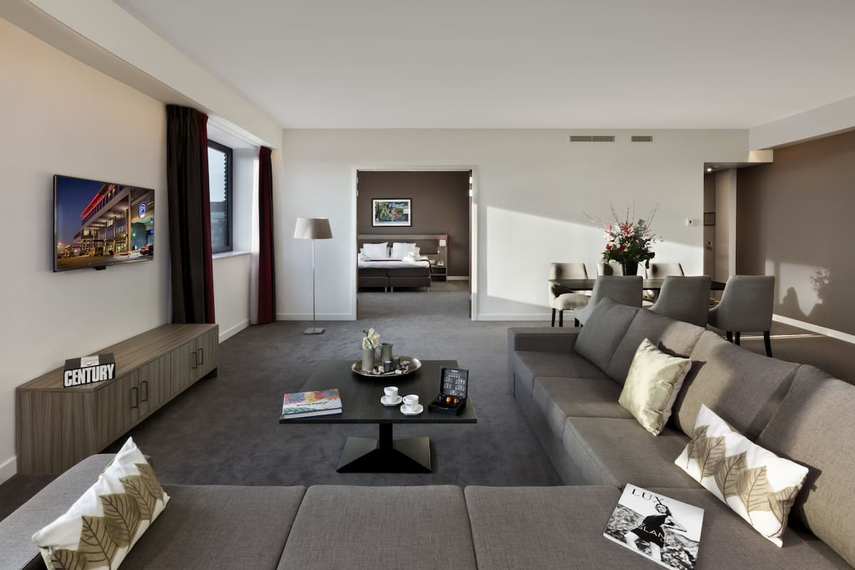 Ein modernes Hotelzimmer mit einem grauen Sofa, einem Couchtisch und einem Essbereich mit Tisch und Stühlen.