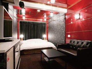 A modern bedroom with a bed, a TV, a desk, and a leather sofa.