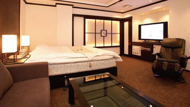 Een hotelkamer met een bed, een televisie, een massagestoel en een bureau met een lamp.