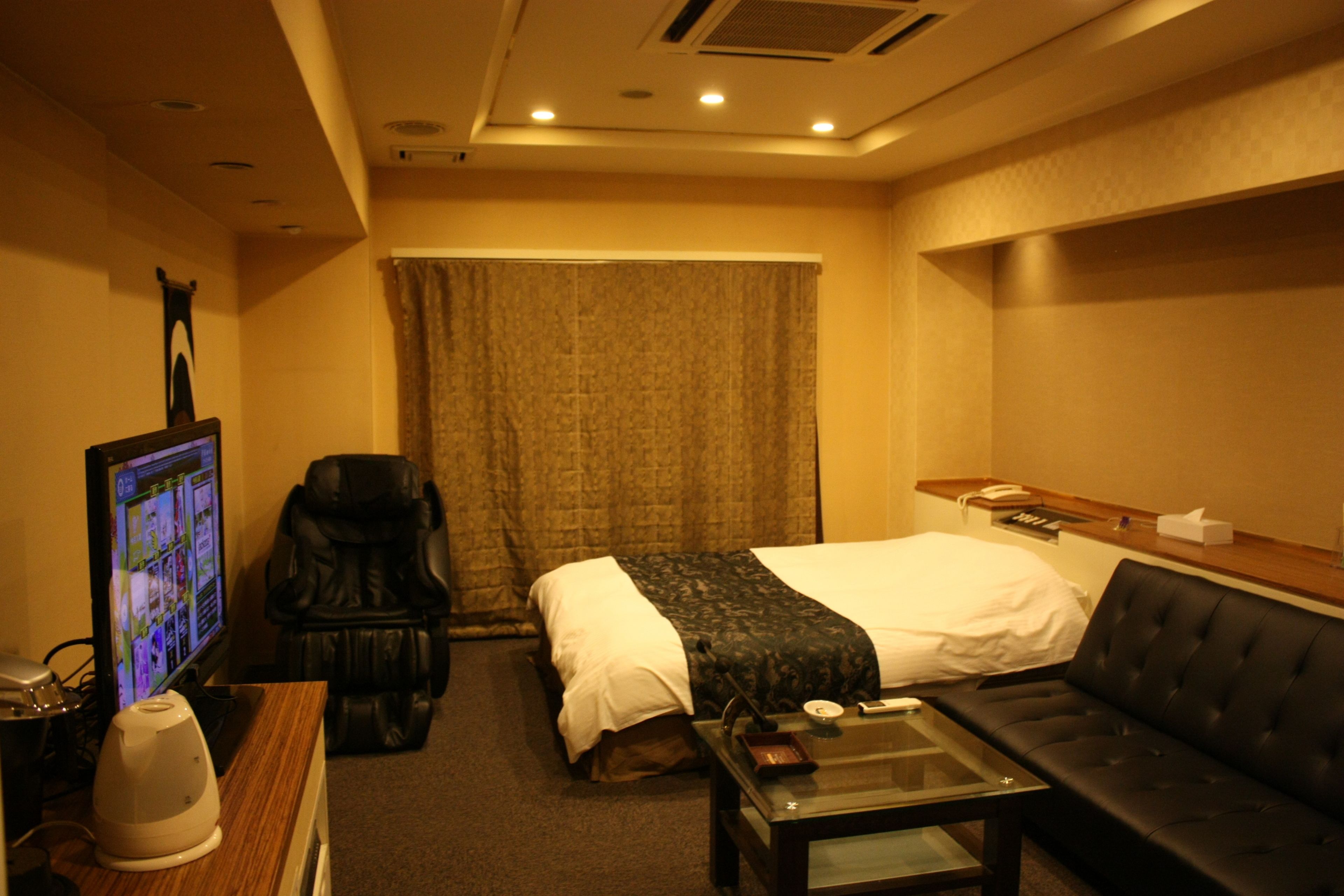 Habitación de hotel con cama, televisión, sillón de masaje, sofá y una pequeña mesa.
