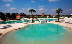 A large outdoor swimming pool with clear blue water, surrounded by lounge chairs and umbrellas.