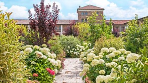A garden pathway leading to a building with a red-tiled roof and multiple windows. - Chervò Residence San Vigilio (Pozzolengo)