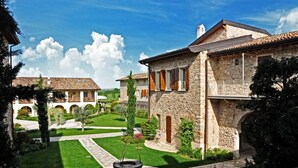 A stone building with a courtyard, a circular stone fountain, and a view of the surrounding landscape. - Chervò Residence San Vigilio (Pozzolengo)
