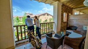 A balcony with wicker furniture and a golf bag, overlooking a garden and buildings. - Chervò Residence San Vigilio (Pozzolengo)