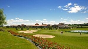 A golf course with a clubhouse, a pond, and red flowers in the foreground. - Chervò Residence San Vigilio (Pozzolengo)