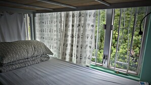 Une chambre à coucher avec un lit, des rideaux ornés de motifs végétaux, une fenêtre donnant sur un paysage verdoyant et une table de chevet avec une lampe.