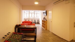 Une pièce avec une table de baby-foot, un canapé rouge et un téléviseur fixé au mur.