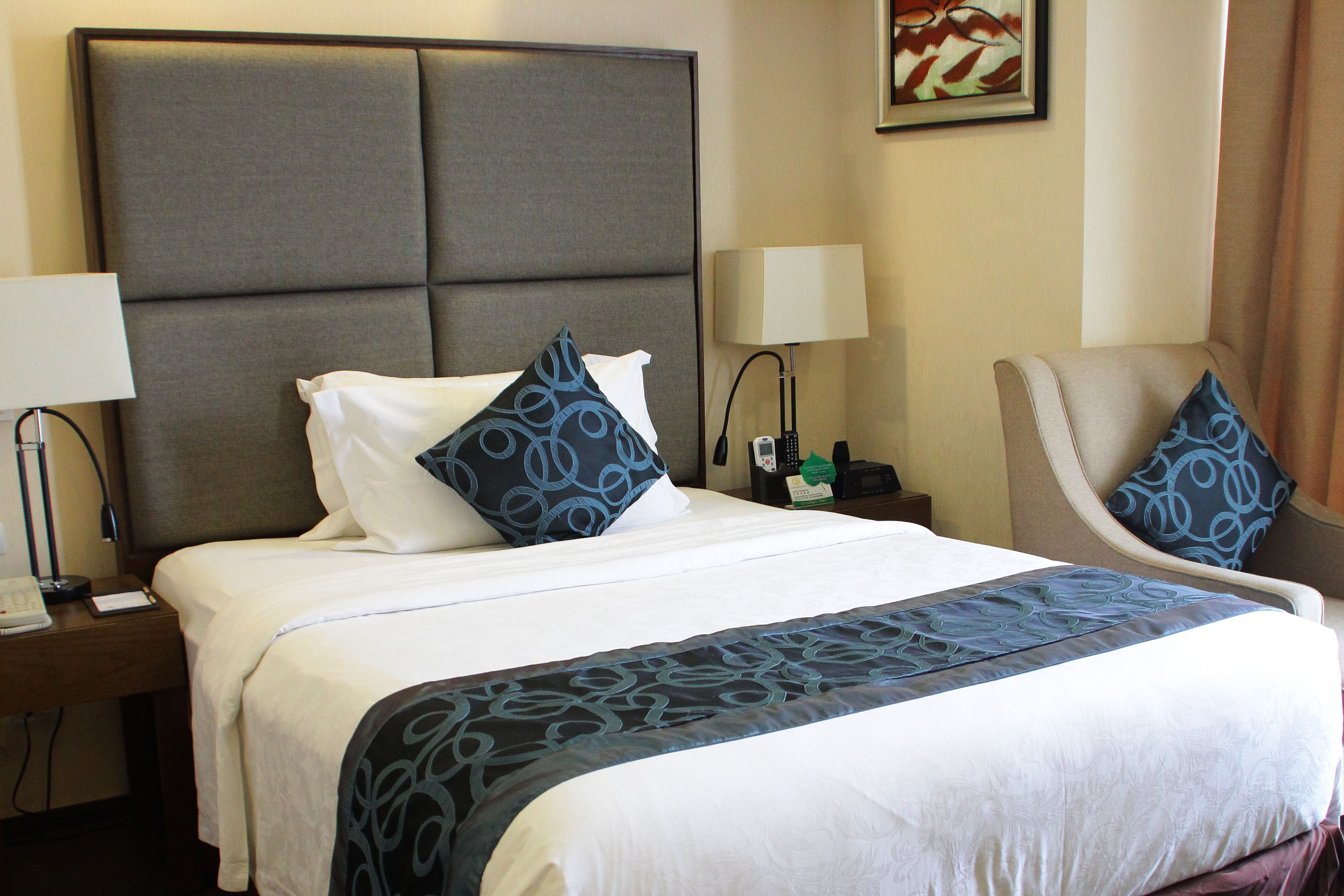 A hotel room with a large bed, two bedside tables, a chair, and a lamp.